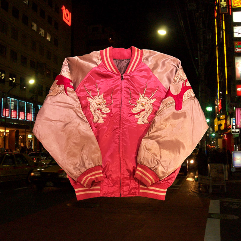 This a photo of the same bright pink jacket from front view. On the front there is embroidery of two happy dragon faces
    on the side lapel panels of the jacket.